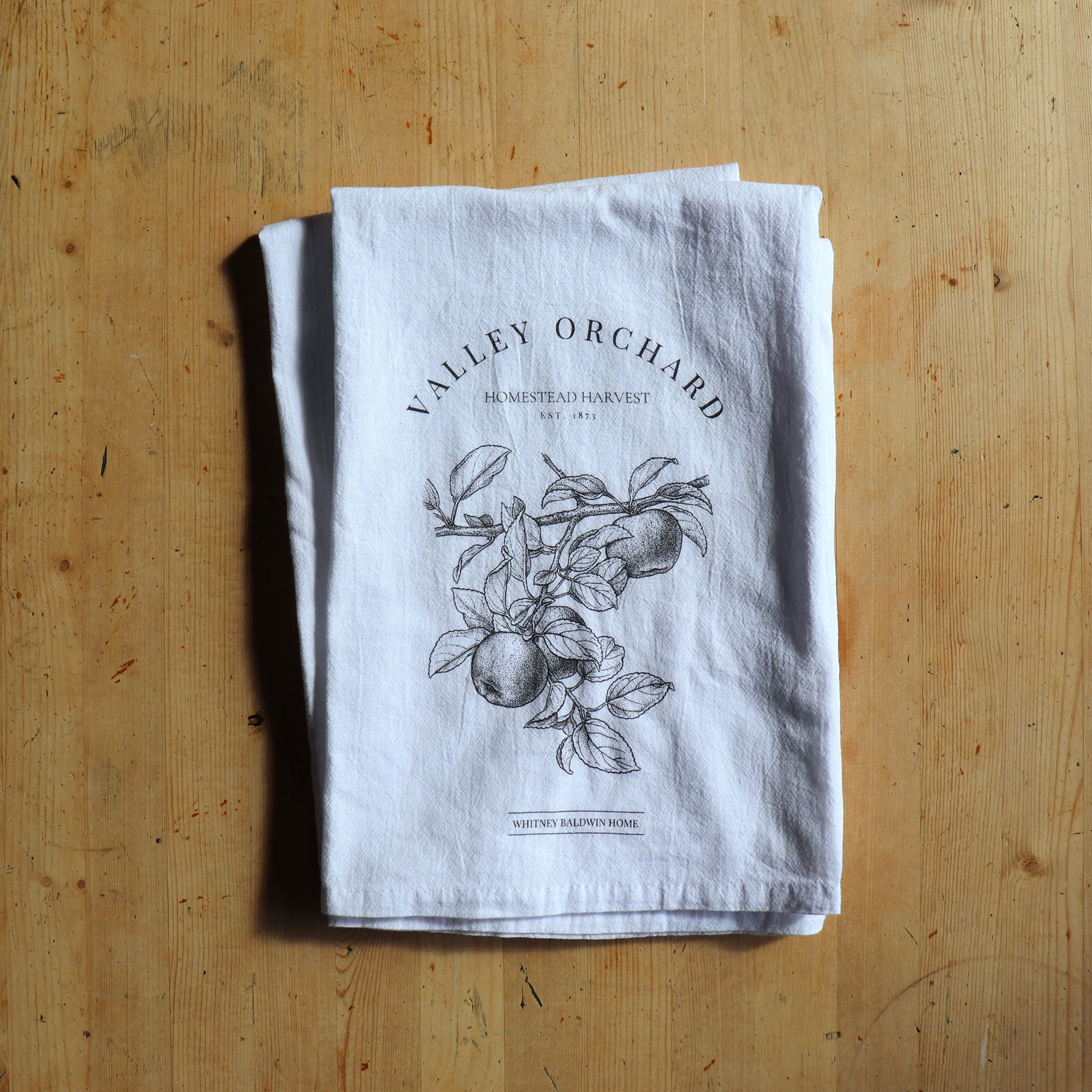 homestead harvest valley orchard apple orchard tea towel. Tea towel in a stack with other tea towels form the homestead harvest collection.