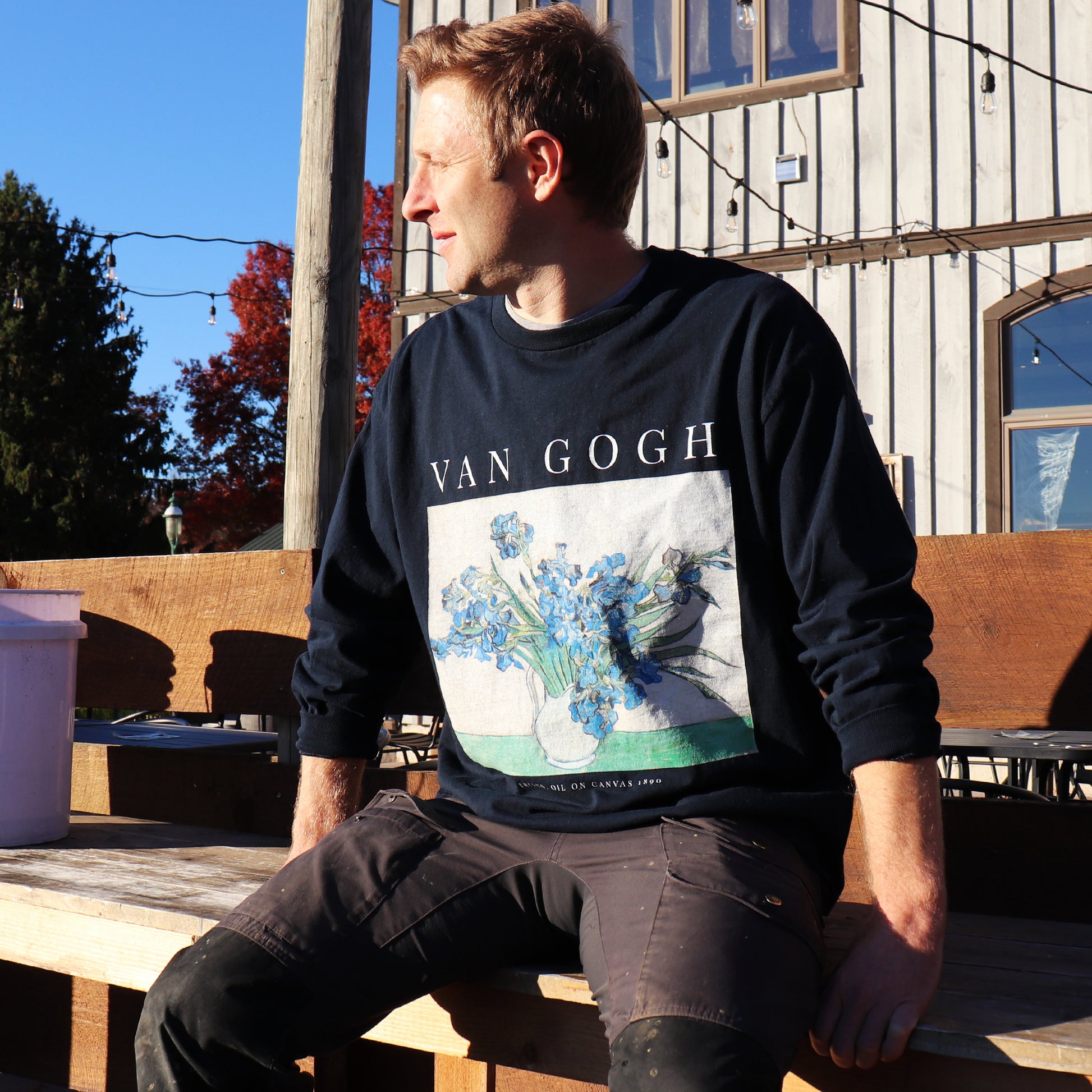 rustic man sitting outside of winery wearing navy long sleeve vincent van gogh t-shirt looking into the sunset