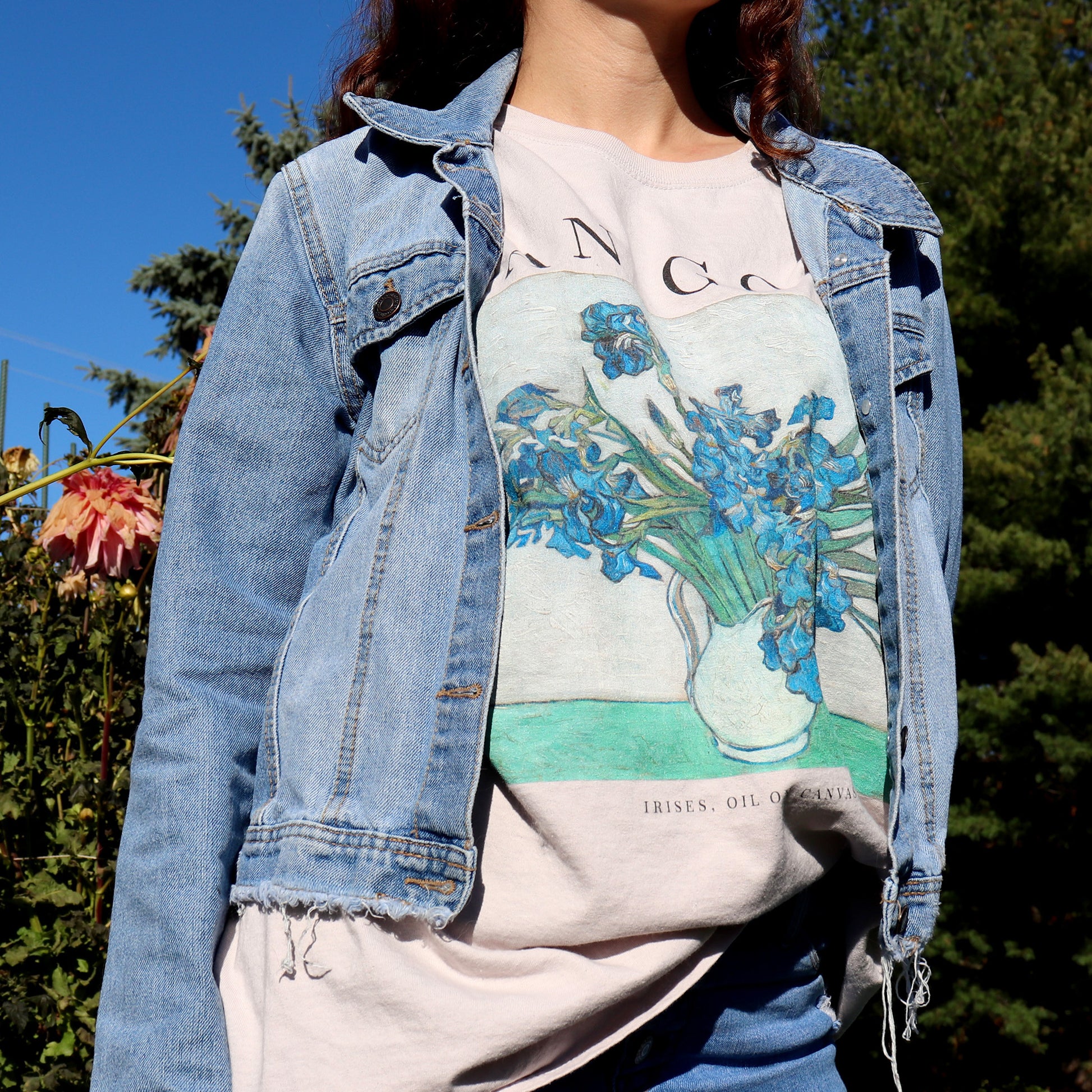 woman standing in a flower field wearing vincent van gogh irises tshirt in the color sand and a denim jacket