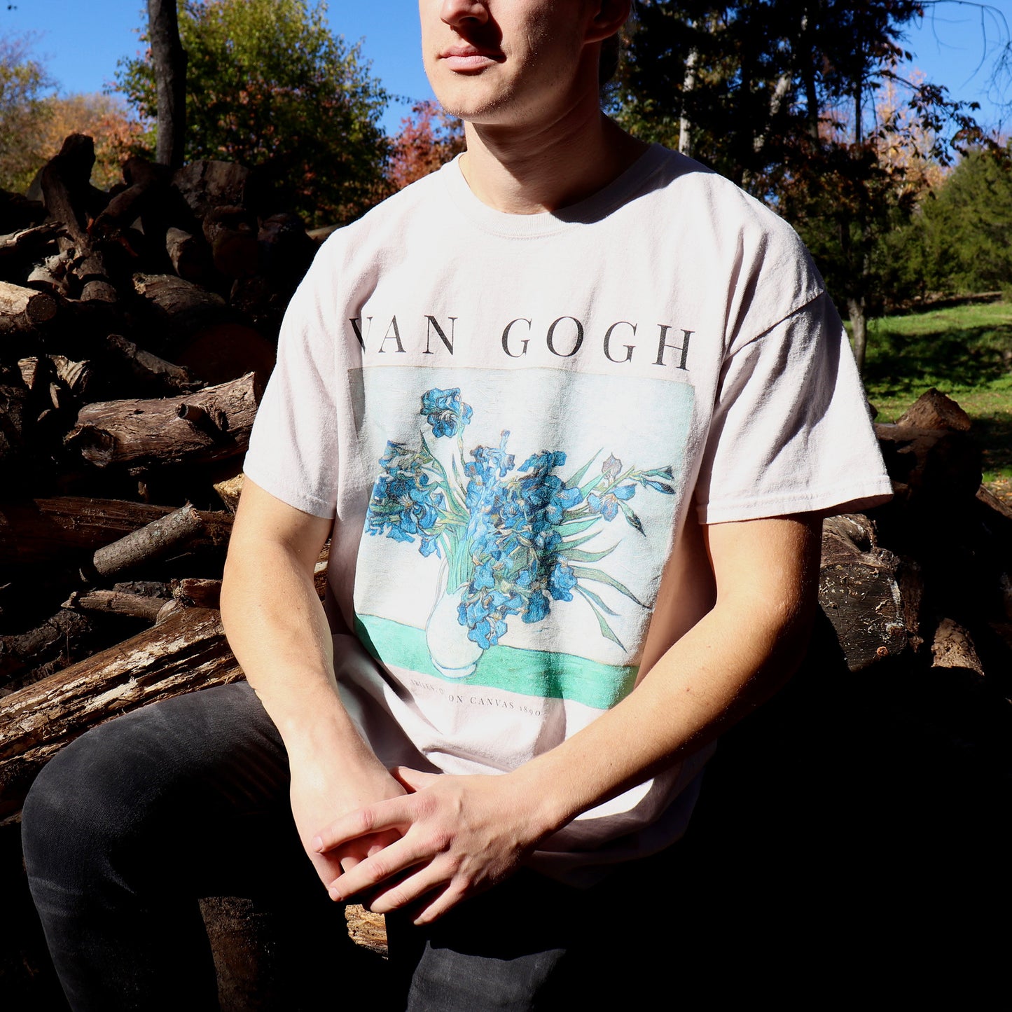 Man sitting near a wood pile wearing vincent van gogh irises tshirt in the color sand