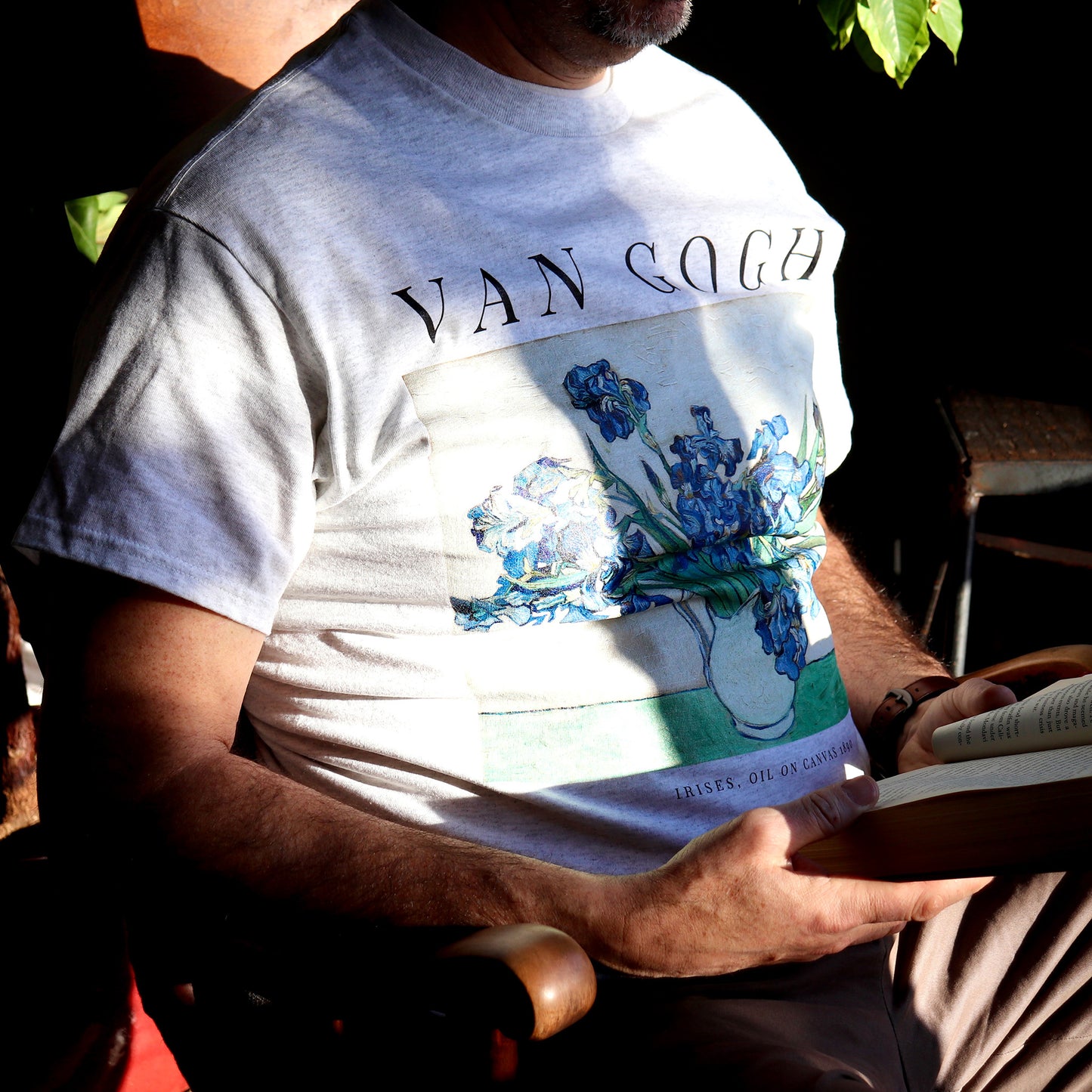 man sitting in rocking chair reading a book wearing the vincent van gogh irises t shirt in the color ash by whitney baldwin home