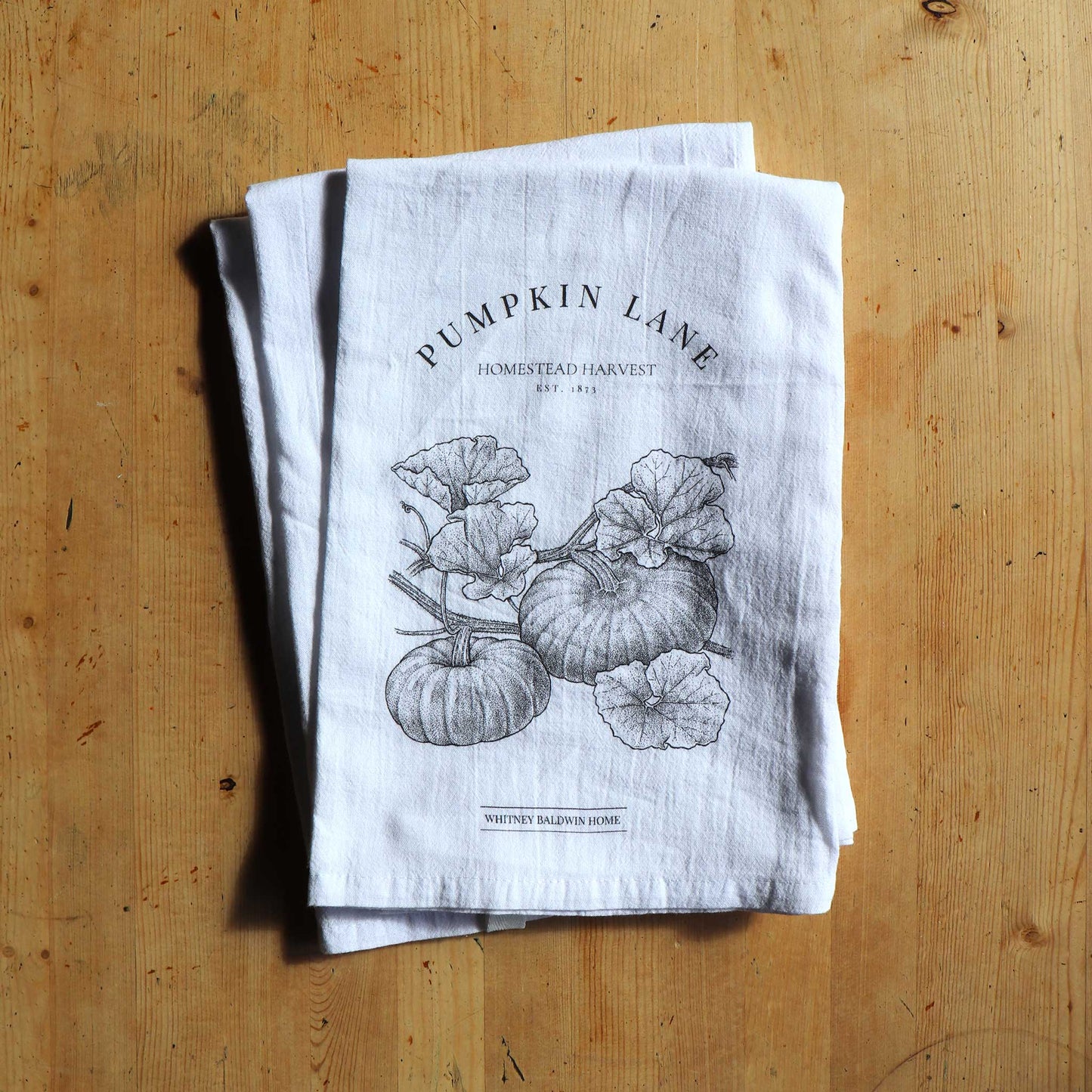 Homestead Harvest Pumpkin Lane Tea Towel. This pumpkin patch tea towel is stacked on top of the other teatowels in this collection