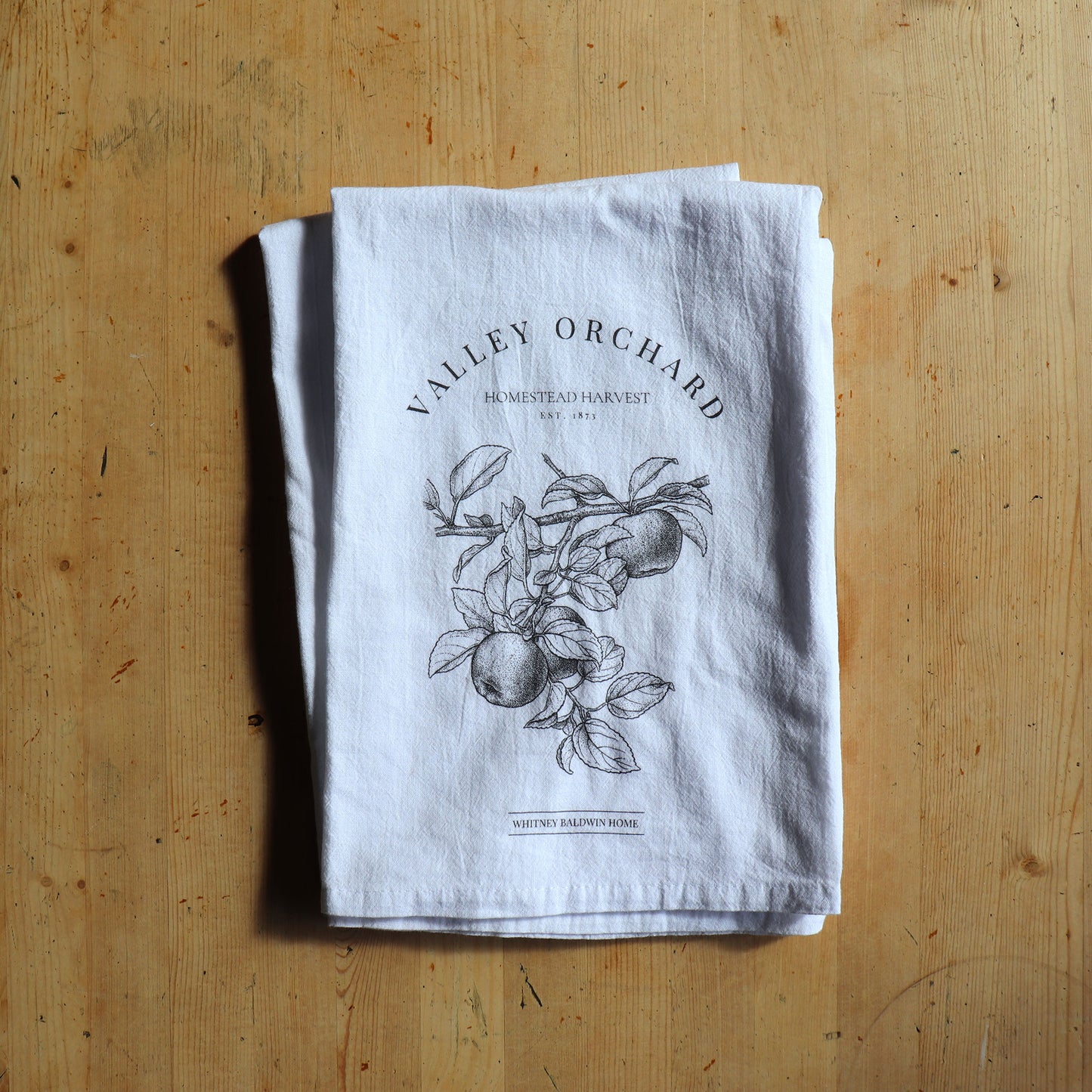 homestead harvest valley orchard apple orchard tea towel. Tea towel in a stack with other tea towels form the homestead harvest collection. 